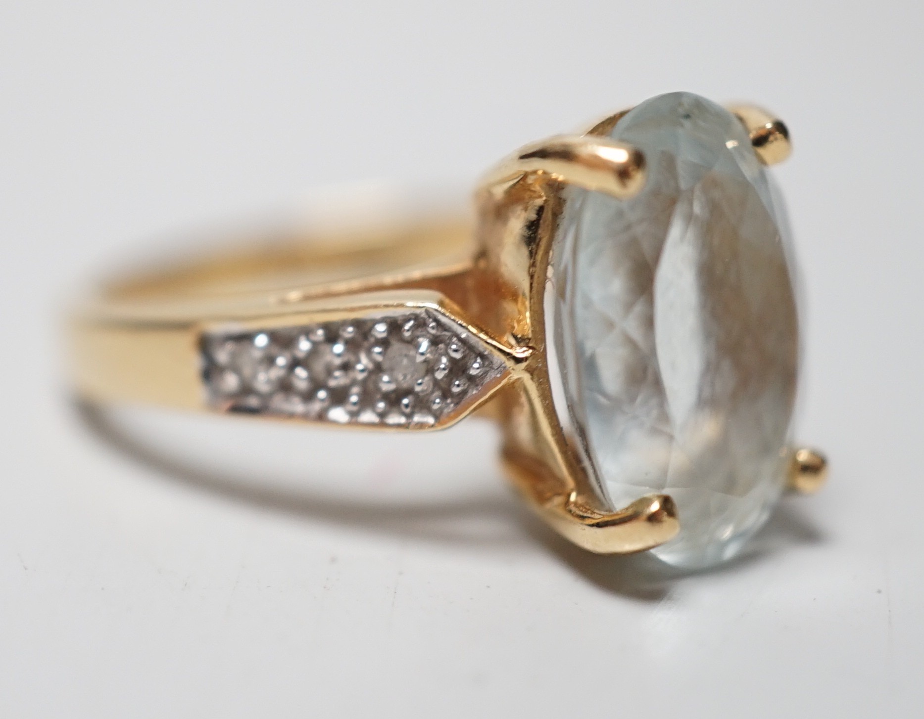 A modern 18ct gold and oval cut aquamarine set dress ring, with diamond chip set shoulders, size N, gross weight 5.5 grams.